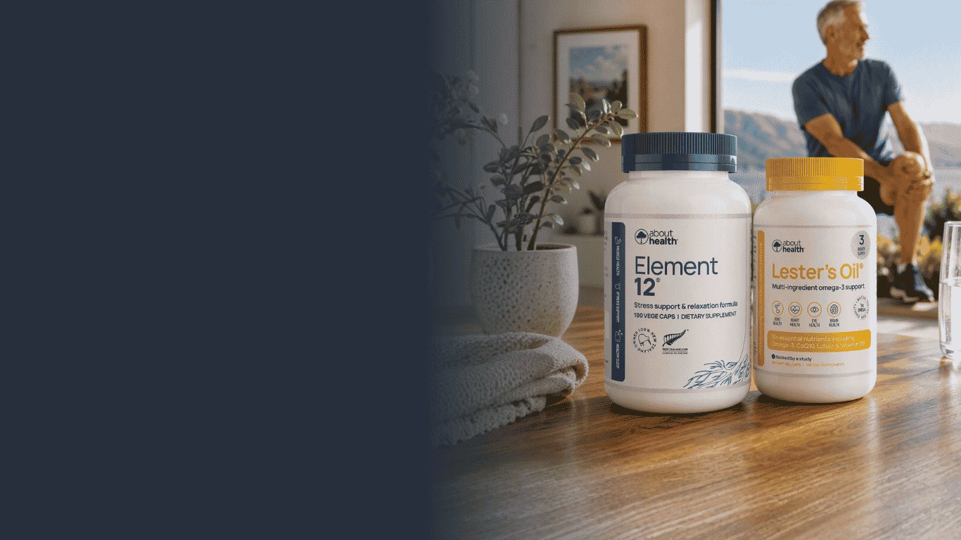 Two white supplement bottles from Health Hero sit on a wooden table in a bright indoor setting. The bottle on the left is labeled 'Element 12' with a dark blue cap, and the bottle on the right is labeled 'Lester's Oil' with a yellow cap.