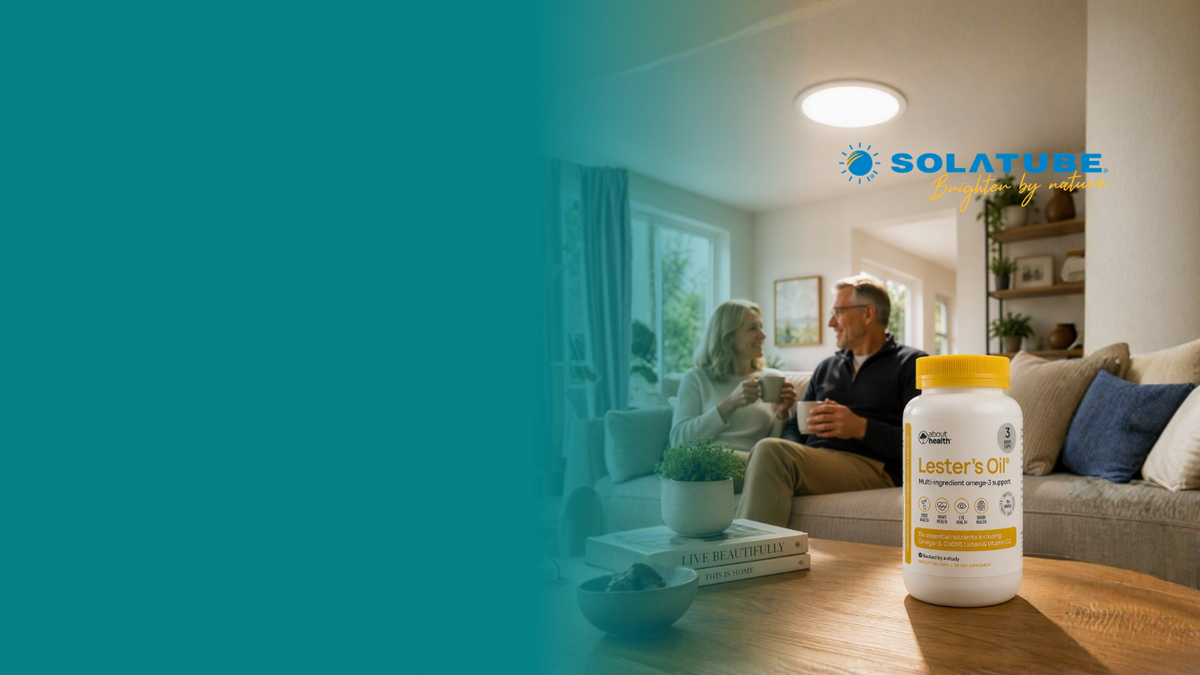 A white bottle of Lester's Oil with a yellow cap sits on a wooden table in a cozy living room setting, with a couple sitting on a sofa in the background. A large teal graphic overlay covers the left side of the image, and the Solatube brand logo is visible in the upper right.