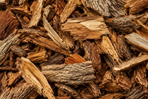 A close-up view of natural wood willow bark chips or mulch pieces in warm brown and tan tones, filling the entire frame.