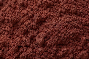 A close-up texture shot of a fine, granular red grape seed powder in a deep reddish-brown color.