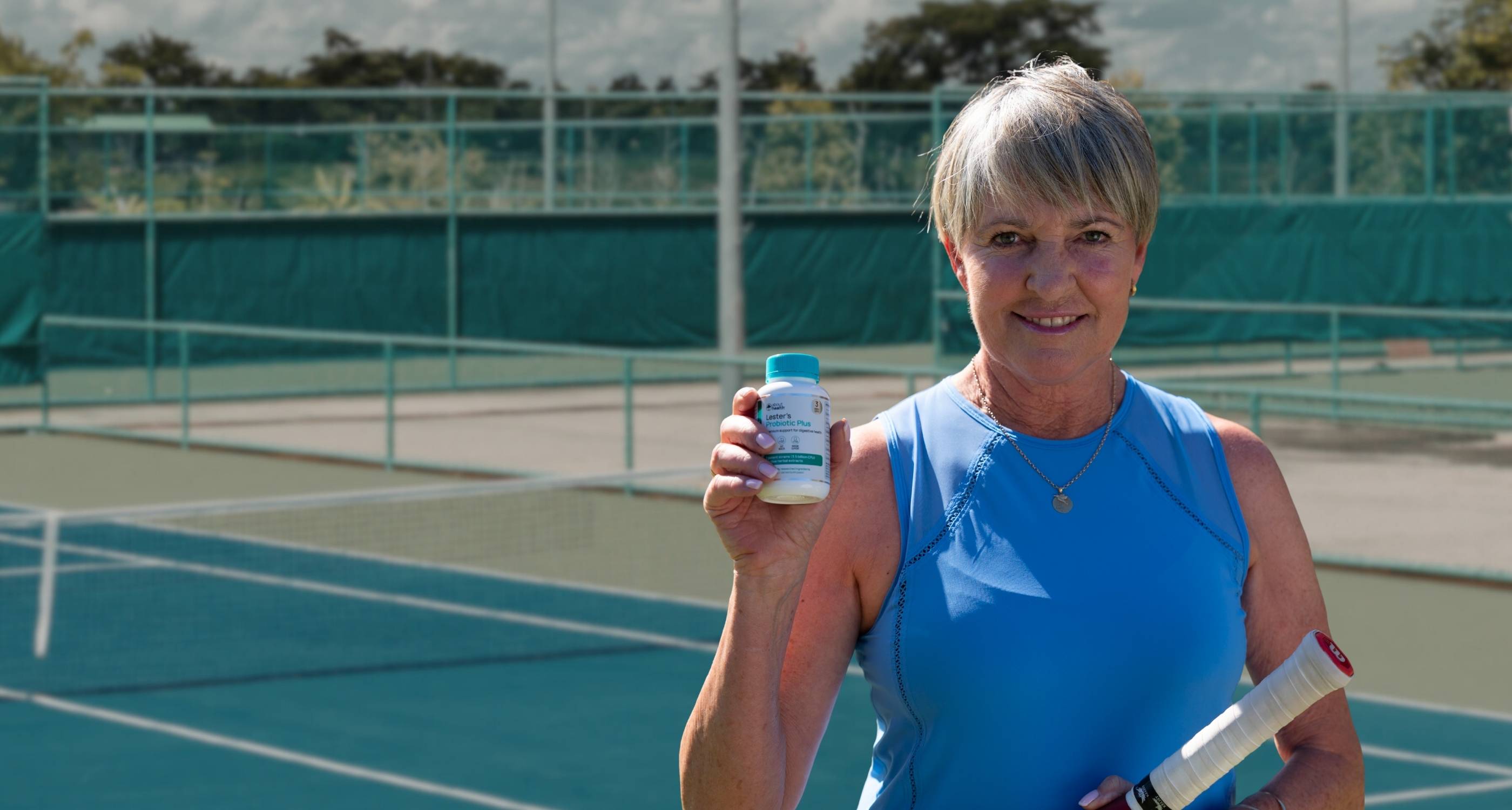 Woman holding a probiotic supplement bottle on a tennis court