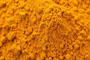 A close-up of a mound of bright orange-yellow ground turmeric powder with a textured, granular surface.