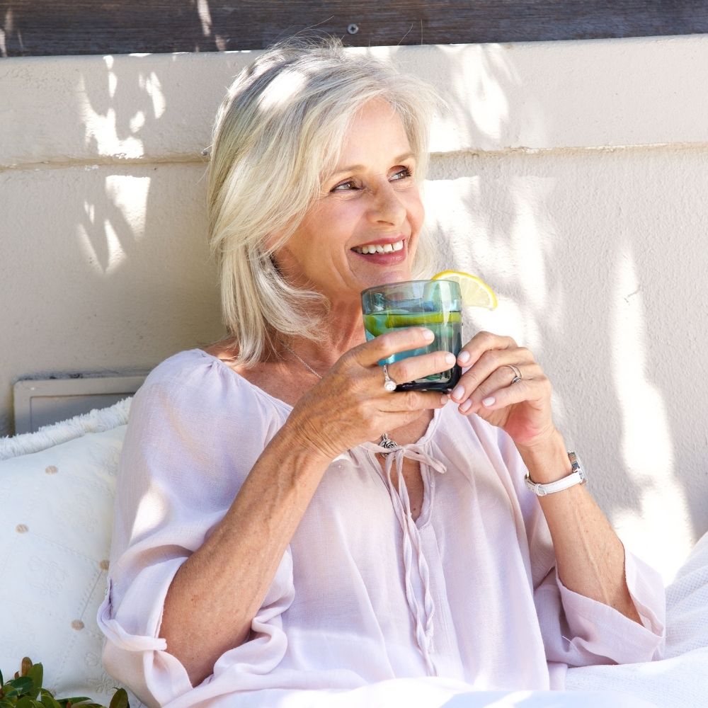 Woman sitting outdoors, feeling relaxed after using lester's night cap and drinking water.