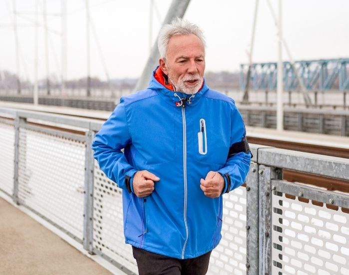 Man in a blue jacket running on a bridge.