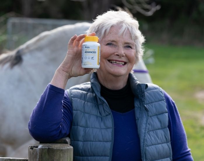 Elder woman holding Lester's Oil Advanced with horse in the background